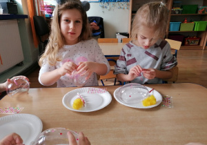 Dziewczynki ozdabiają kwiatuszkami akrylowe jajko.